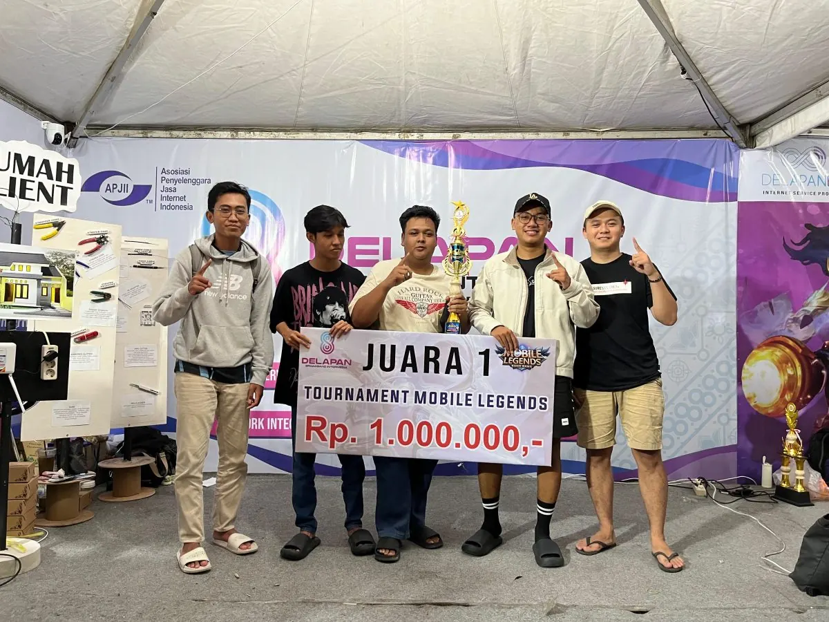 Tim pemenang Juara 1 Turnamen Mobile Legends DelapanBit berfoto bersama memegang piala dan banner hadiah utama