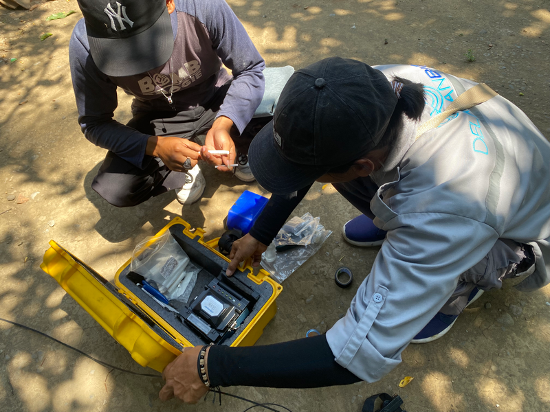 Teknisi melakukan splicing serat optik di pinggir jalan dengan pelindung terpal