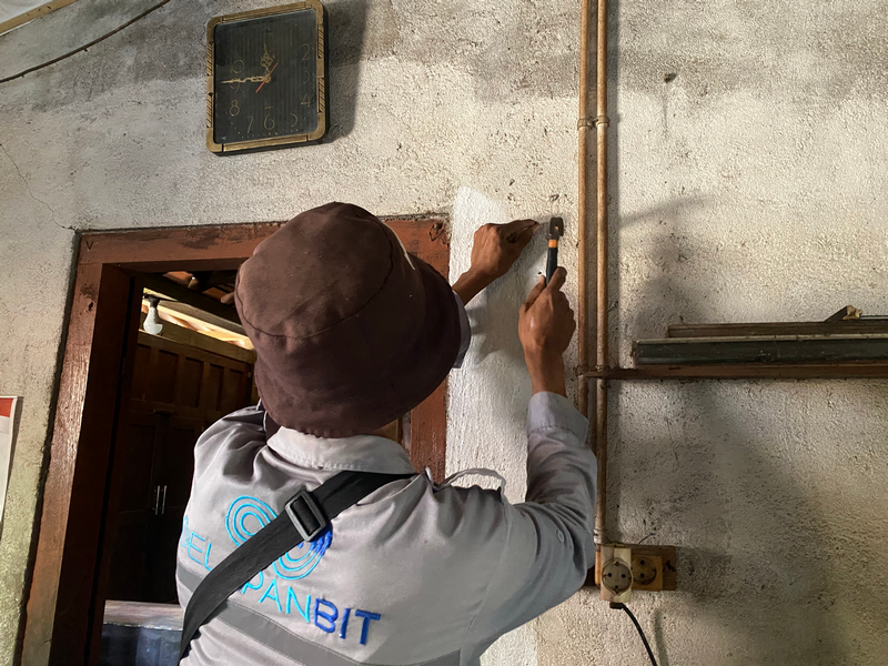 Teknisi merapikan jalur kabel fiber optik di dinding dalam rumah pelanggan