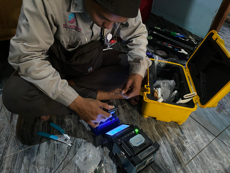 Teknisi menyambung kabel serat optik menggunakan alat splicer